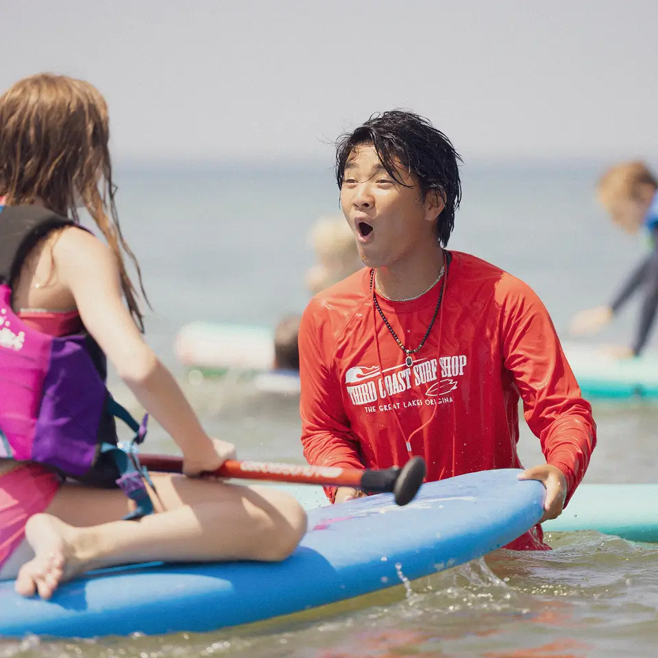 excited beach camp instructor helping kids surf