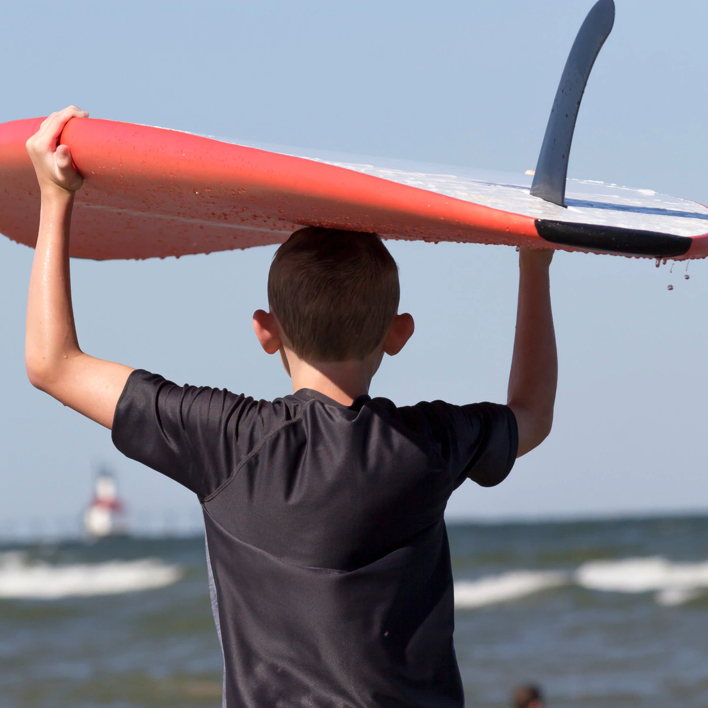 young boy carry surfboard overhead